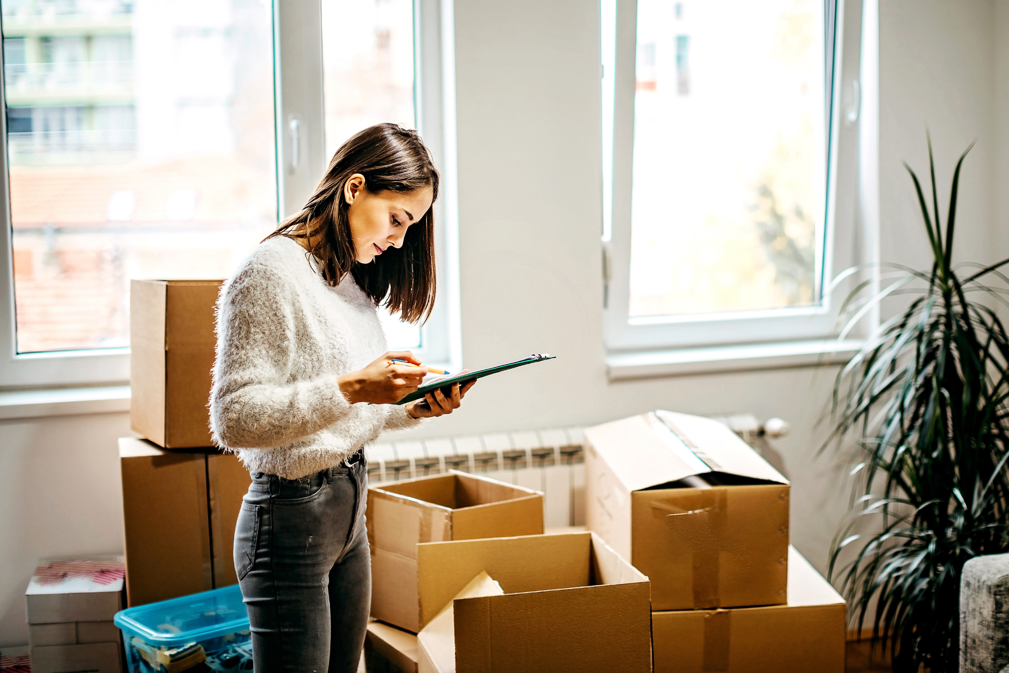 Woman reading notes from a clipboard surrounded by moving boxes.